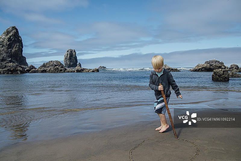 男孩在沙滩上用木棍在沙地上圈图片素材
