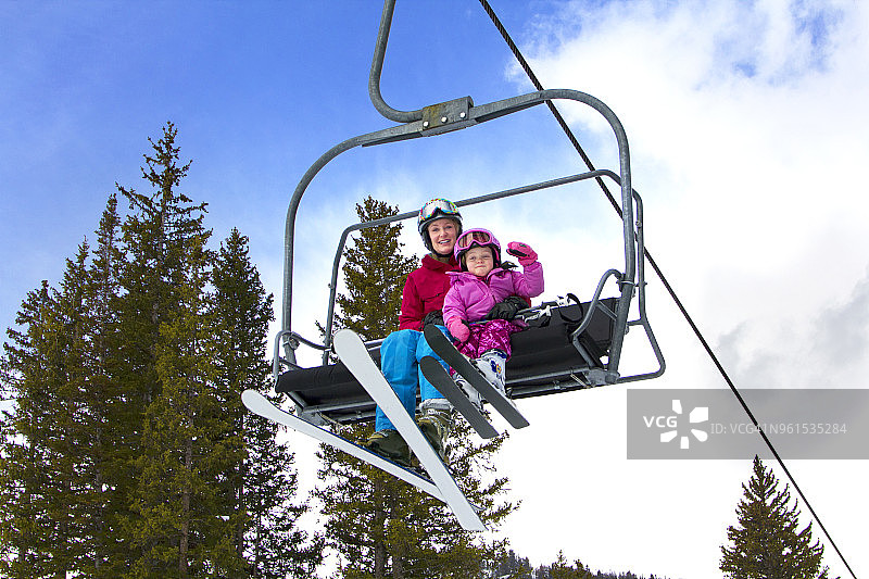 低角度的母亲和女儿坐在滑雪缆车对着天空图片素材