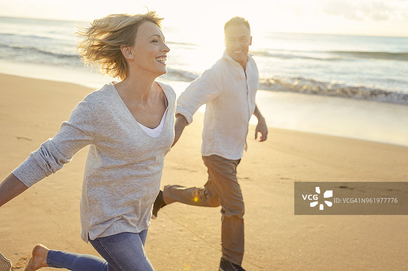 成熟的夫妇在日落或日出时在海滩上跑步。图片素材