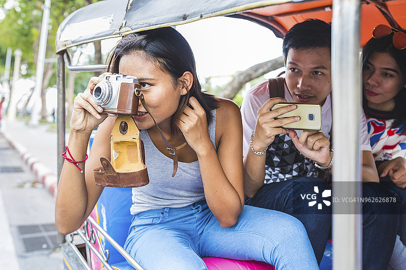 泰国，曼谷，三个朋友骑着嘟嘟车用智能手机拍照图片素材