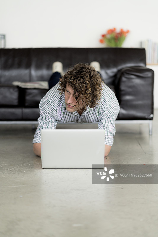 一个商人一边做平板支撑，一边用笔记本电脑在家工作图片素材