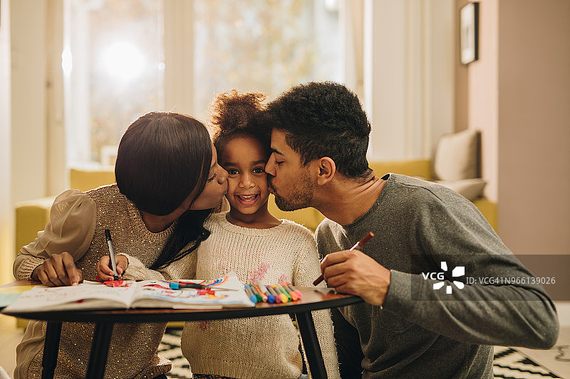慈爱的黑人父母在创作时间亲吻他们的女儿。图片素材