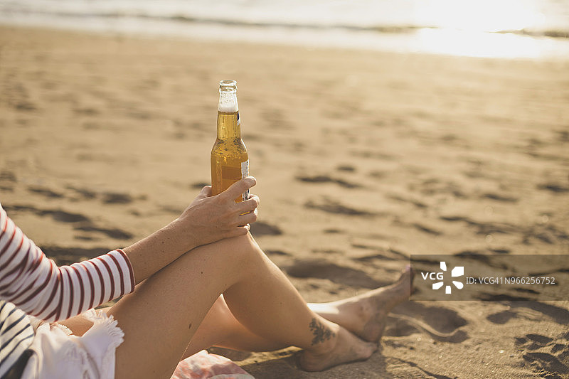 女人拿着啤酒瓶在海滩放松的低部分图片素材