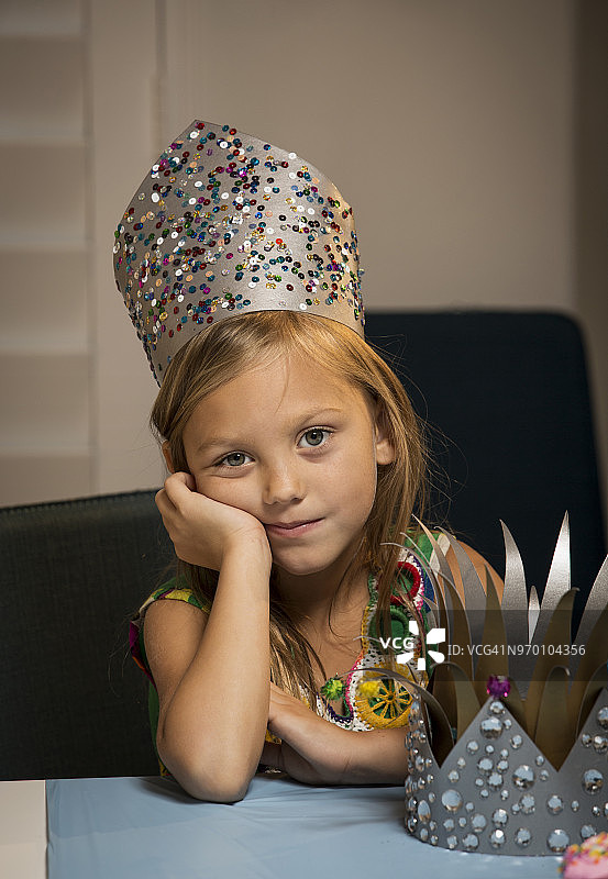 戴着皇冠的女孩坐在家里的桌子旁图片素材