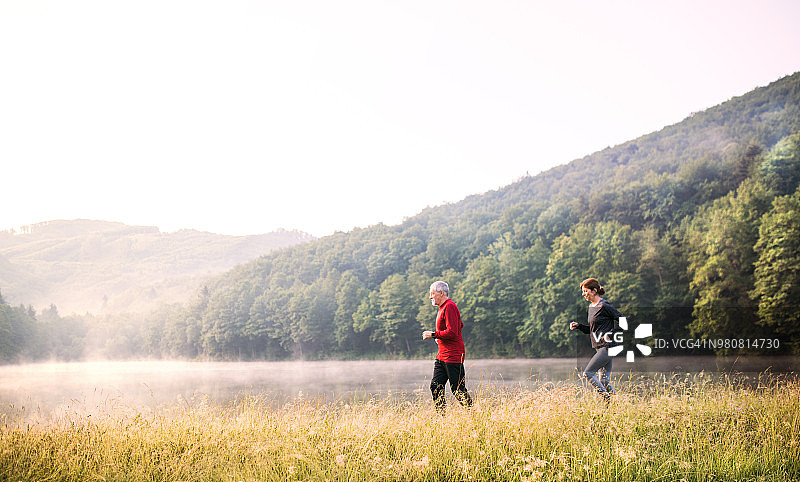 有雾的清晨，一对老年夫妇在户外的湖边跑步。图片素材