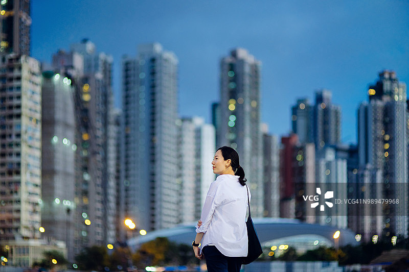 美丽的亚洲女人看着发光的金融摩天大楼，享受壮观的城市夜景图片素材