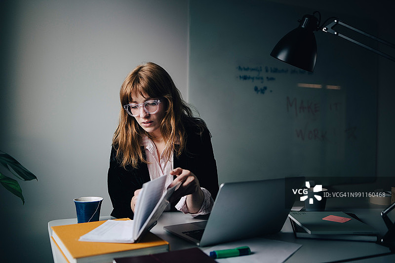 自信的年轻女商人坐在创意办公室里用笔记本电脑阅读文件图片素材
