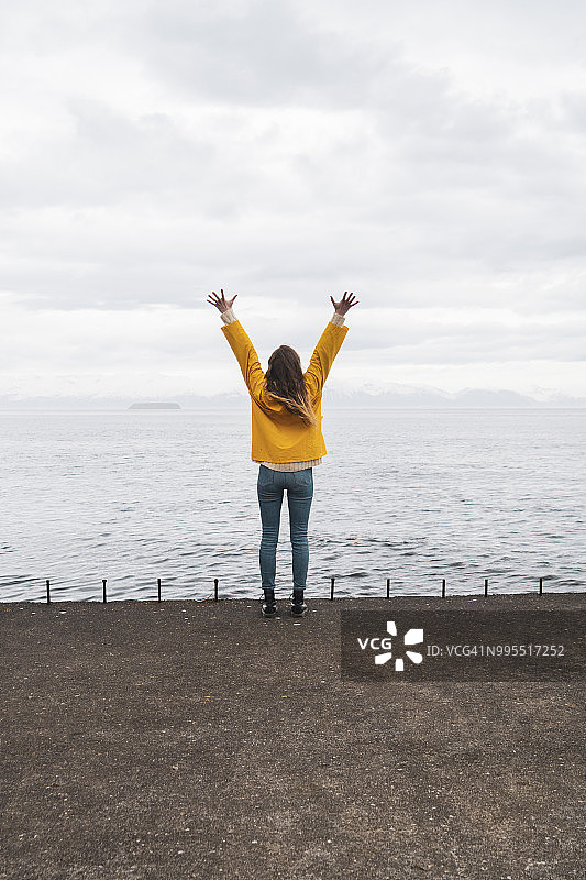 冰岛，一名女子高举双臂站在海边图片素材