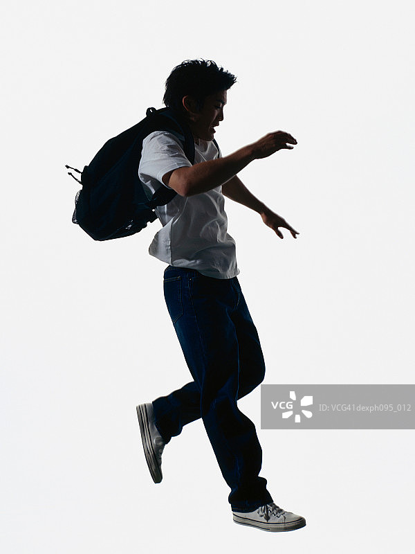 年轻的亚洲人穿着牛仔裤和t恤，背着背包，在半空中跳图片素材