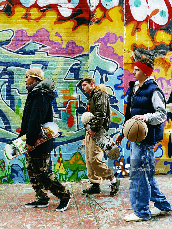 三个十几岁的男孩走在一个城市设置滑板，篮球和态度图片素材