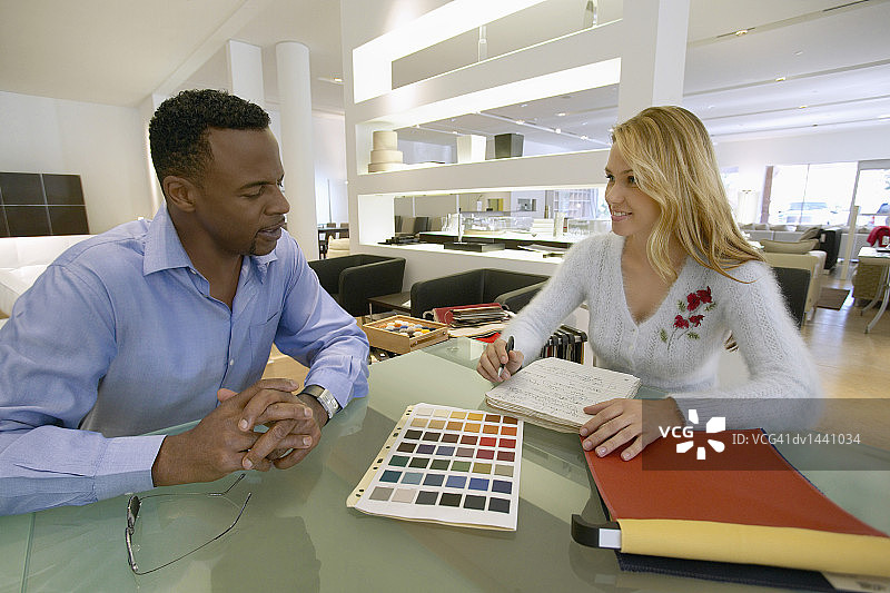 在一家室内设计店里，一名男子坐在桌子旁与一位女店员讨论彩色图表图片素材