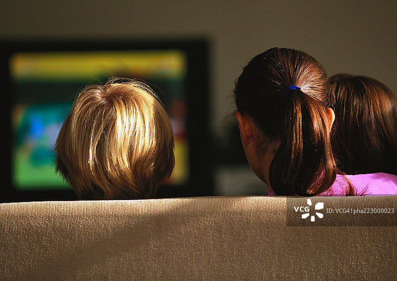 年轻的男孩和女孩坐在沙发上看电视。图片素材