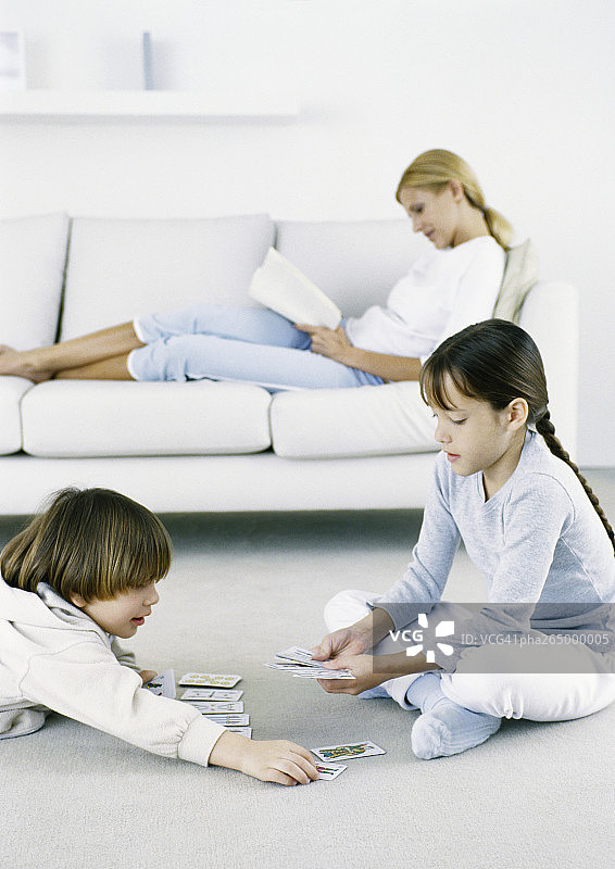 女孩和男孩在地板上打牌，女人坐在沙发上看书图片素材