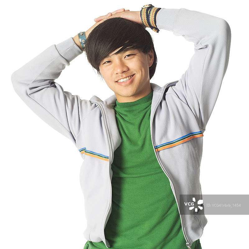 一个穿着绿色衬衫和运动衫的亚洲男性少年把他的手放在头上，微笑着图片素材