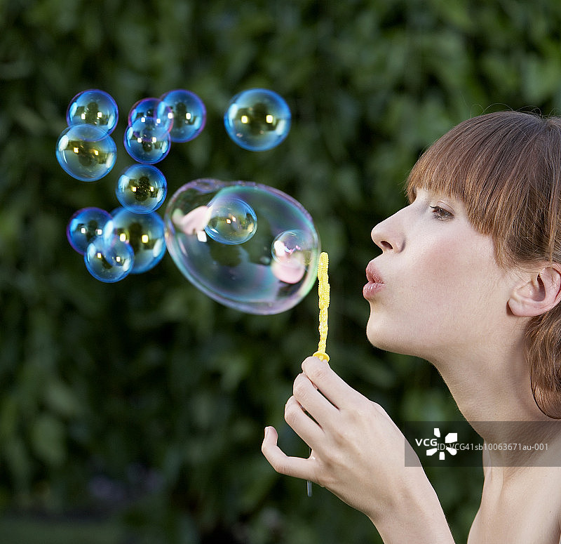 年轻女子在室外吹泡泡，侧视图图片素材