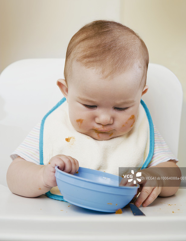 女婴(6-7个月)拿着碗坐在高椅子上图片素材