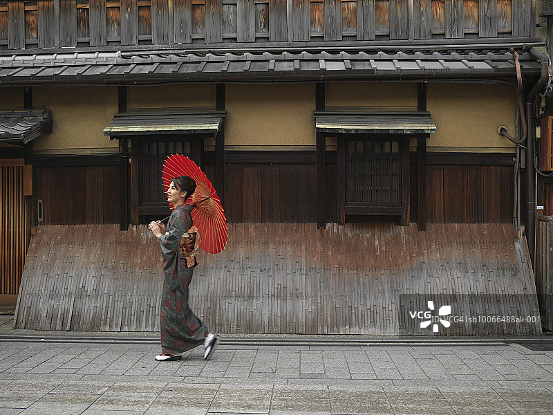 日本，京都，祗园，身着和服的女子拿着红色油纸伞，走在大街上图片素材