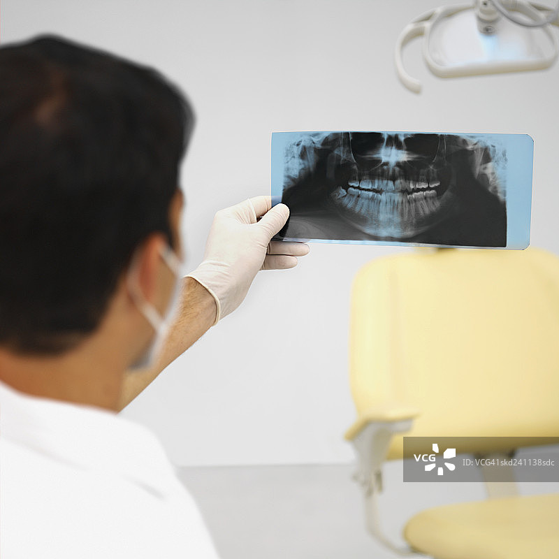 牙科医生佩戴外科口罩和手套及检查x光片的后视图图片素材