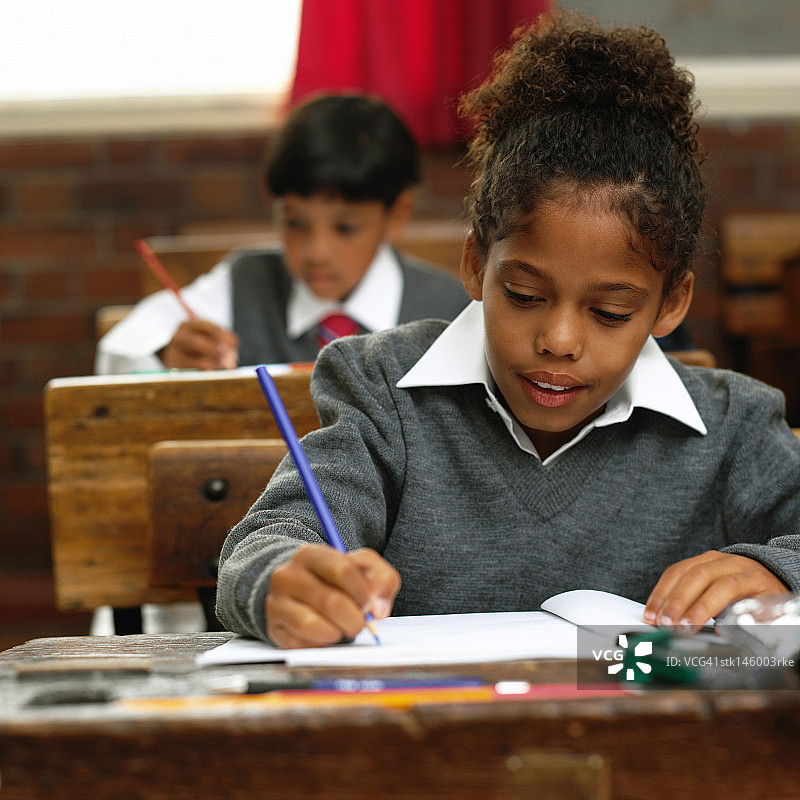一个年轻女孩在学校用铅笔写字的肖像图片素材