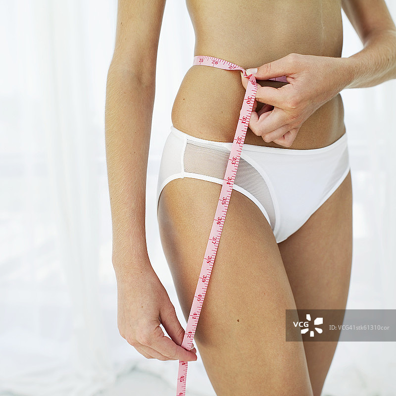 一个女人用卷尺测量她的腰的特写中间部分图片素材