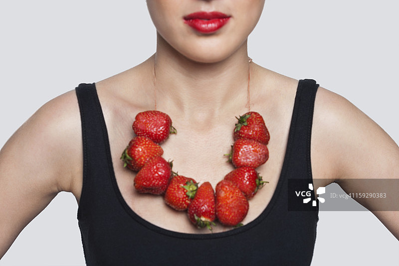 在灰色背景上戴着草莓项链的女人的中间部分图片素材