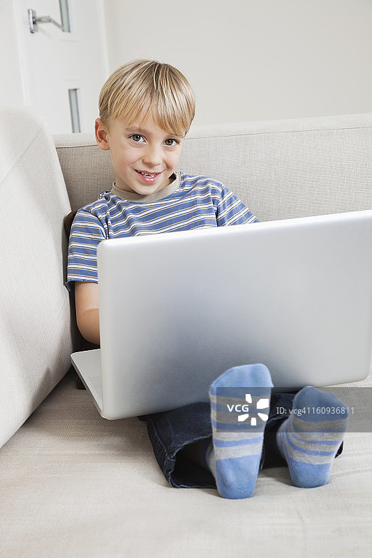 一个快乐的小男孩在沙发上用笔记本电脑图片素材
