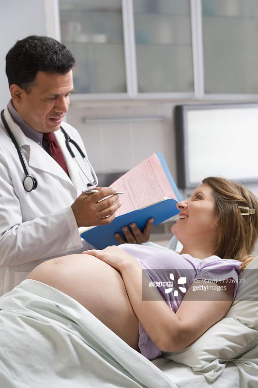 男医生与躺在医院病床上的孕妇交谈图片素材