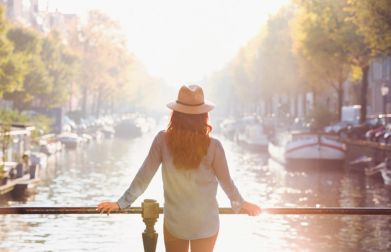 戴着帽子的女人看着阳光明媚的秋天运河的景色，阿姆斯特丹图片下载