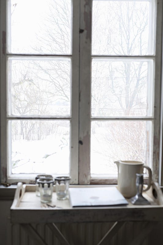 水壶和玻璃杯放在窗户下面的小桌上，可以看到白雪覆盖的花园图片素材