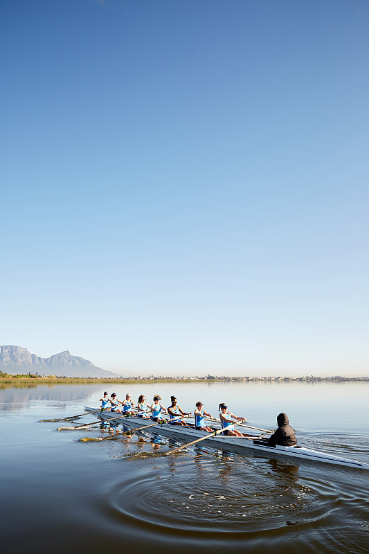 蓝天下，女子桨手在宁静的湖面上划桨图片素材