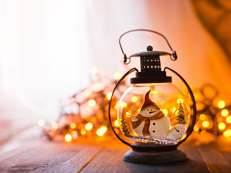 玻璃灯笼与燃烧的蜡烛，圣诞礼物和一个发光的花环在木桌子上图片下载