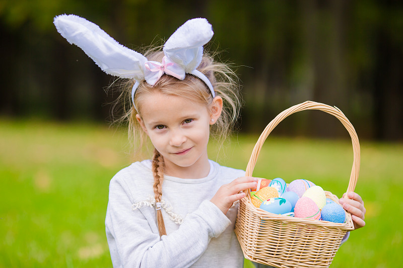 小女孩的肖像戴着兔子耳朵，拿着复活节彩蛋篮子图片素材
