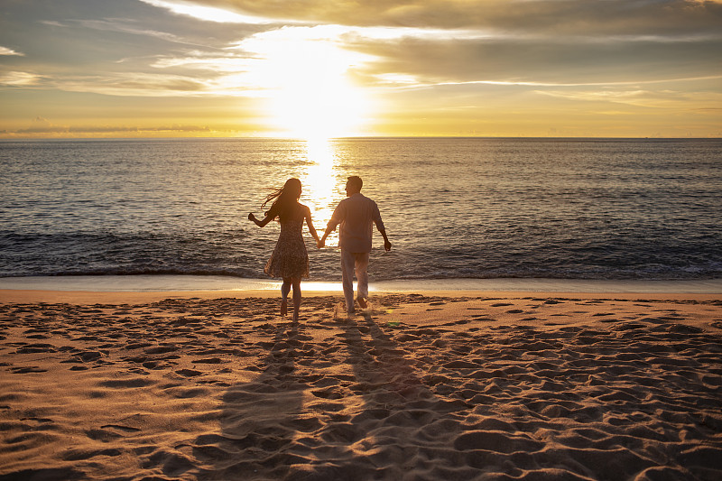 快乐的年轻夫妇在沙滩奔跑图片下载