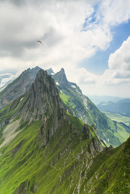 在瑞士阿彭策尔内罗登的一个多云的夏天，从舍弗勒看到陡峭的岩石山峰桑蒂斯的滑翔伞图片下载