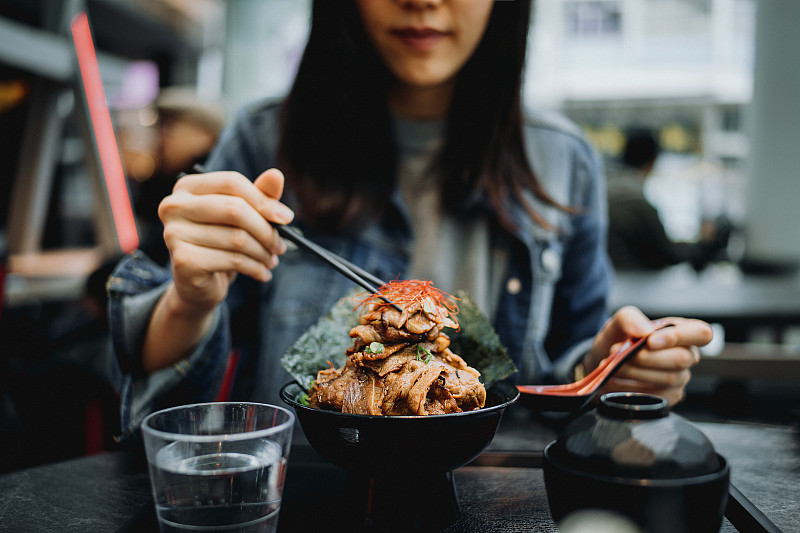年轻的亚洲妇女在日本餐馆愉快地用筷子吃烤牛肉饭碗图片下载