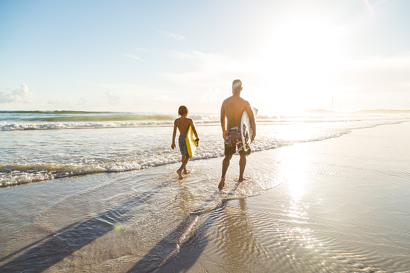 父亲和儿子一起在沙滩上冲浪图片下载