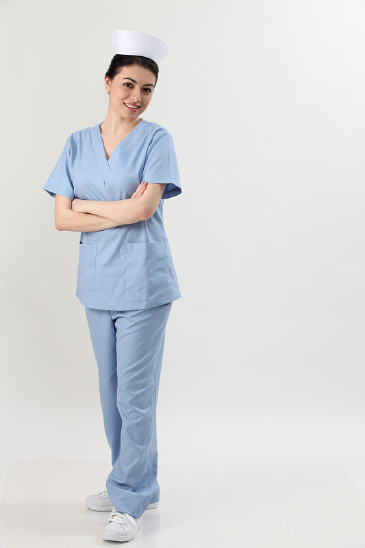 自信的年轻女护士站立双臂交叉的灰色背景的全长肖像图片素材