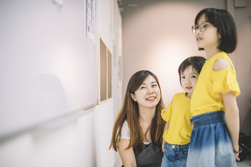 一位亚裔华裔女美术老师给她的两个学生展示白板上的样品，让他们开始画画和绘画活动图片下载