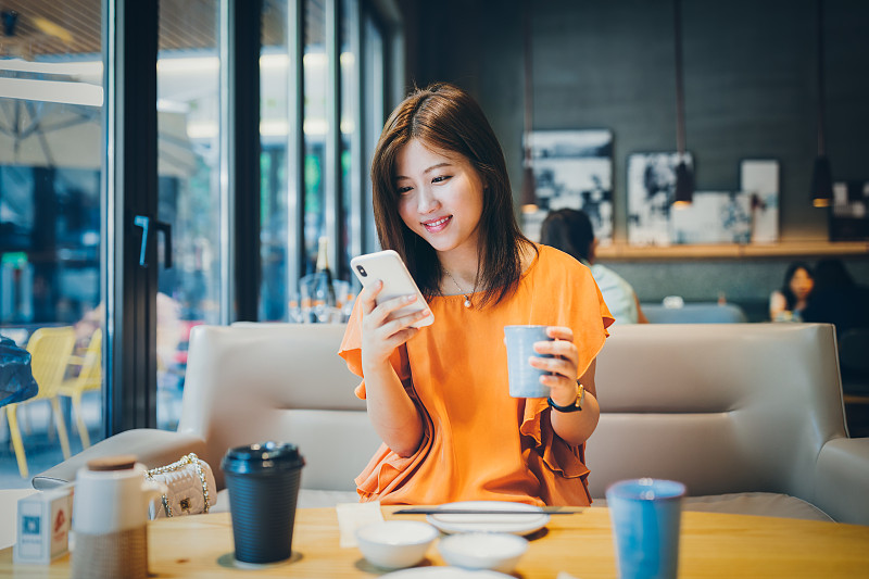 年轻的亚洲女性使用智能手机做生意，网上购物，转账，金融，网上银行。在咖啡店咖啡店模糊的背景。图片下载