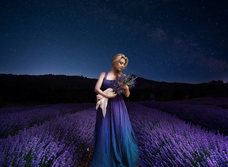 一个手持鲜花的年轻女子，站在田野上，夜深人静图片素材
