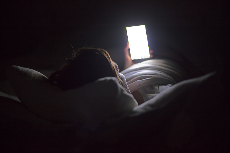深夜躺在床上用智能手机搜索社交媒体的女人，上网成瘾。图片下载