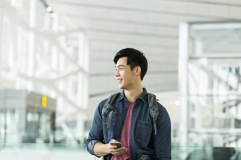 青年男子背着包使用手机在机场等候图片素材