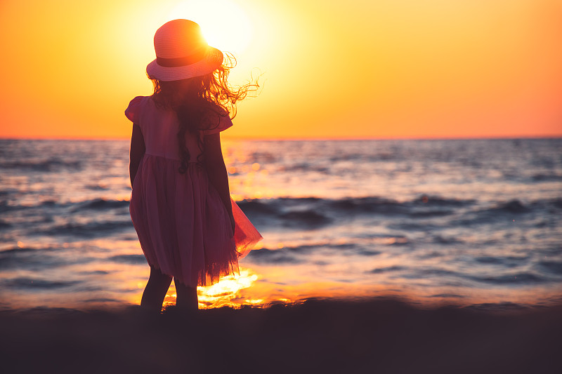 小女孩(6-7)穿着粉红色的裙子在沙滩上看日出图片素材