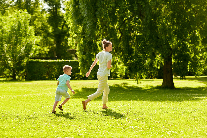 家庭、休闲和人的概念——快乐的妈妈和小儿子在夏季公园里奔跑和玩接球游戏。母亲和儿子在夏季公园玩接球游戏图片素材