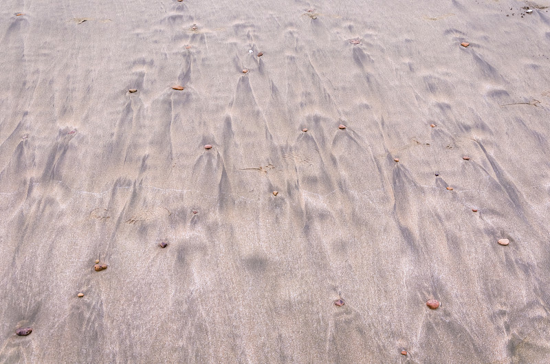 海浪冲刷后黄色海滩上石子后部形成的流水痕迹排列图案图片素材