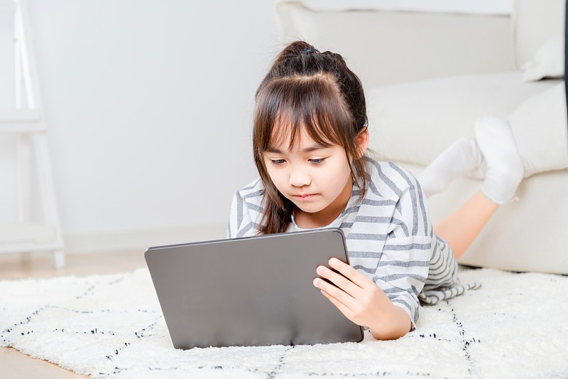 趴在地毯上玩平板电脑的亚洲小女孩图片素材