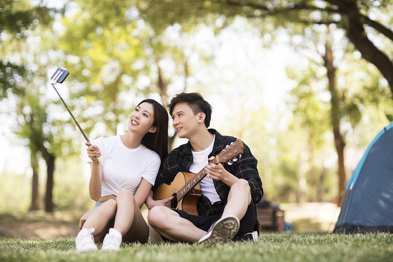 年轻情侣在草地上用手机自拍图片素材