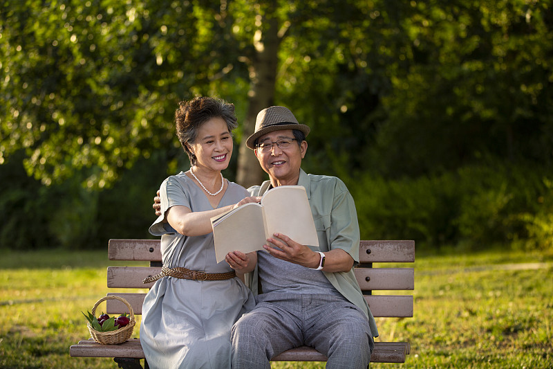 老年夫妻坐在户外公园长椅上休息看书图片素材
