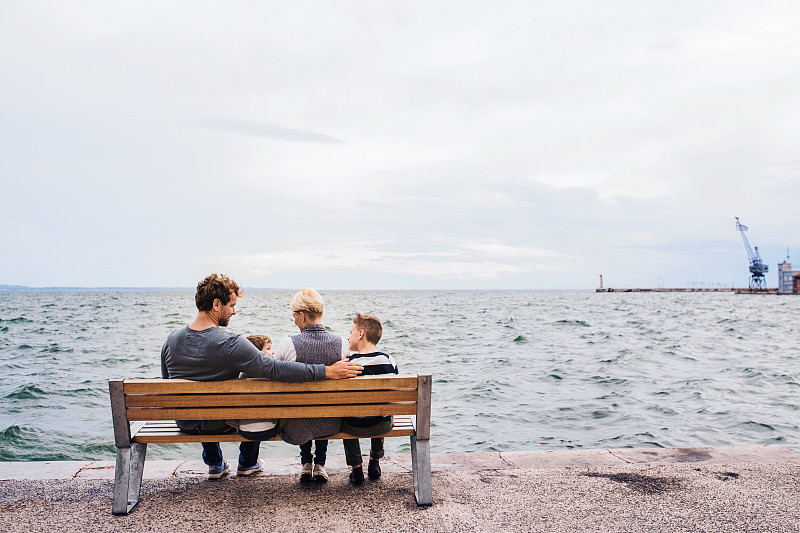 后视图的家庭与两个小孩在户外长椅在海滩上图片素材