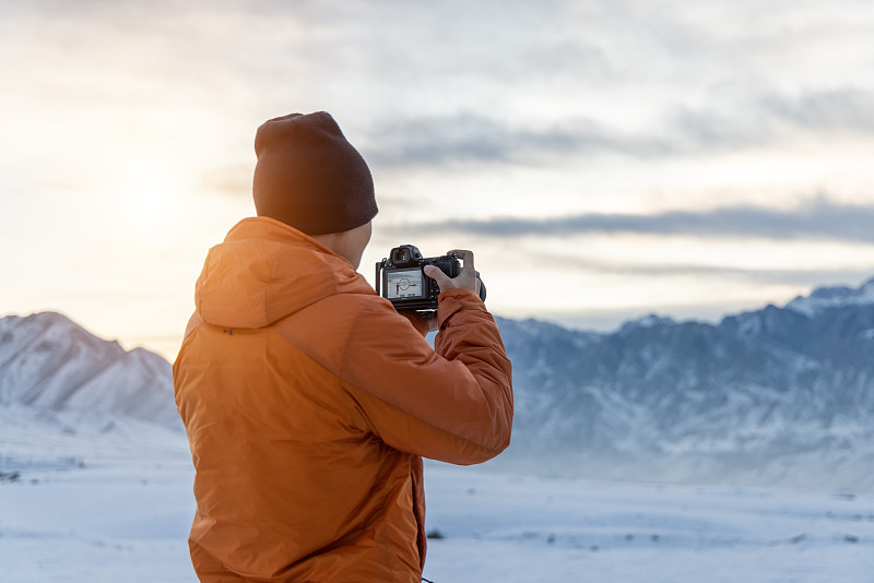 站在白雪皑皑的山上的摄影师的后视图图片下载